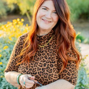 Midwife educator standing outdoors in natural light, smiling warmly while holding essential oil.